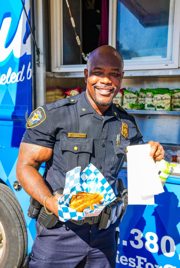 Dallas police officer holding grilled cheese from Ruthie’s For Good food truck catering